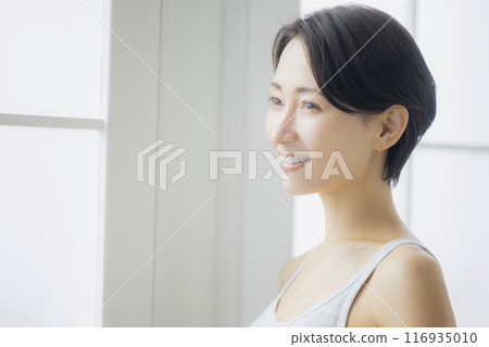 Middle-aged woman looking in the mirror in the living room Middle-aged woman looking in the mirror in the living room 116935010