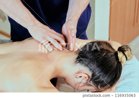 Deep tissue massage for back pain of best therapeutic techniques is performed by trained massage therapist who comes to home of young Caucasian woman. 116935063