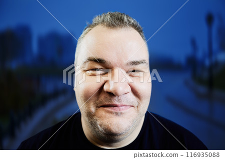 Shy smile of overweight European man in her 40s, face closeup on blue background. 116935088