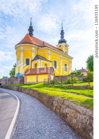 The Church of St. Bartholomew in Pecka, Czechia, is a beautiful example of Baroque architecture. The yellow building features two spires and stands on a hill overlooking the town. 116935195