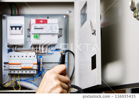 Removal outer jacket of high-voltage cable with retractable utility knife, against background of an electrical panel. Removal outer jacket of high-voltage cable with retractable utility knife, against background of an electrical panel. 116935435
