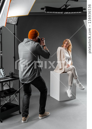 A professional photographer is taking pictures of a fashion model in a studio environment 116936536