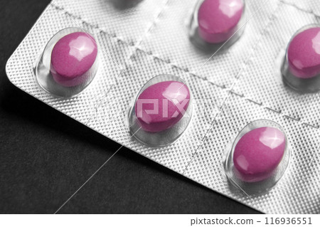 Pink vitamin complex pills in a blister pack with smooth glossy surface of the medication on a black table. Macro shot Pink vitamin complex pills in a blister pack with smooth glossy surface of the medication on a black table. Macro shot 116936551