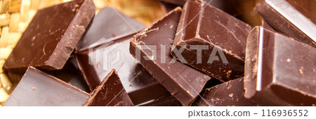 Macro shot of dark bitter broken chocolate pieces in rustic eco friendly wicker bowl. Web banner design element. Organic pure ingredients without additives for healthy eating and baking Macro shot of dark bitter broken chocolate pieces in rustic eco friendly wicker bowl. Web banner design element. Organic pure ingredients without additives for healthy eating and baking 116936552