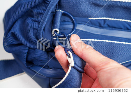 A man's hand fastens the strap carabine of a blue traveler's hiking bag close up 116936562