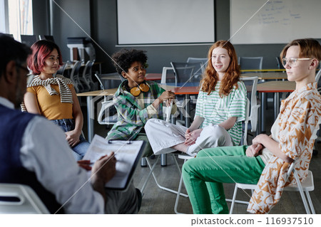 Caucasian teen girl speaking about her feelings and emotions during group therapy session at school, copy space 116937510