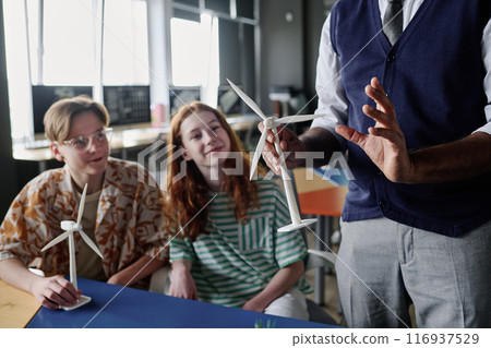 Selective focus shot of unrecognizable teacher holding wind turbine model telling teenagers about renewable energy Selective focus shot of unrecognizable teacher holding wind turbine model telling teenagers about renewable energy 116937529