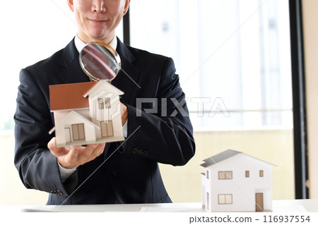 A young man in a suit looking at a model house with a magnifying glass A young man in a suit looking at a model house with a magnifying glass 116937554