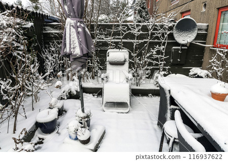 Winter snow-covered garden with garden furniture under the snow. Winter snow-covered garden with garden furniture under the snow. 116937622