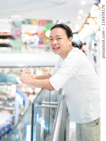 Asian, Thai long hair Man in white t-shirt is standing in the Department store. Asian, Thai long hair Man in white t-shirt is standing in the Department store. 116939176