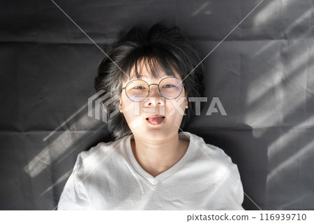Cute short hair - glasses Asian woman laid on black wrinkled cloth background and stick her tongue out. 116939710