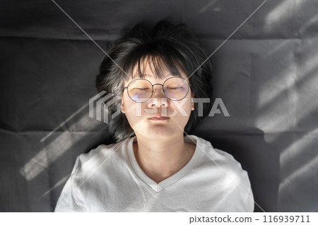 Cute short hair - glasses Asian woman laid on black wrinkled cloth background with window light on her. 116939711