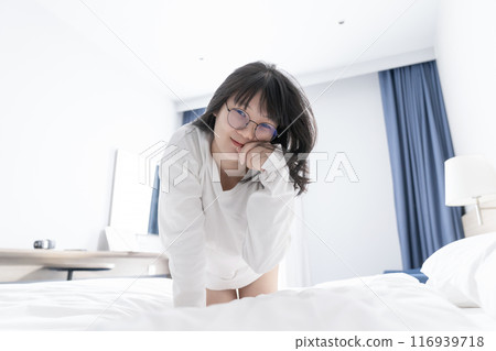 Asian, Japanese, Chinese, Thai woman posed like a cat character whit cute claw action on the bed and looks at the camera. 116939718