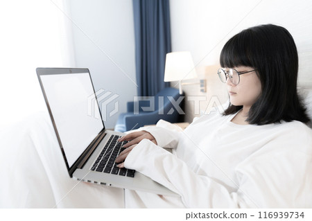 Glasses Asian cute woman works and plays laptop notebook on the bed in Work From Home period. 116939734