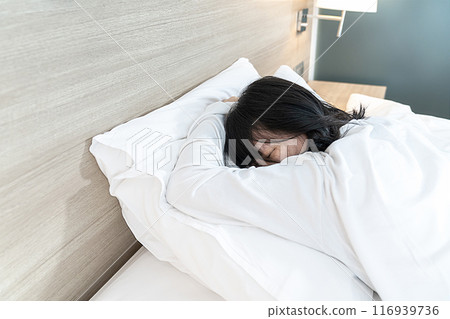 Asian Lady in white long arm t-shirt pajamas lie prone, lie on the stomach in bed with tried and exhausted mood and tone. Asian Lady in white long arm t-shirt pajamas lie prone, lie on the stomach in bed with tried and exhausted mood and tone. 116939736