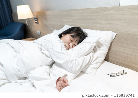 Asian cute young woman in white long arm pajamas lie on her side on the bed 116939741