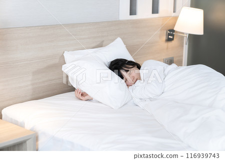 Asian cute young woman in white long arm pajamas lie on her side on the bed Asian cute young woman in white long arm pajamas lie on her side on the bed 116939743