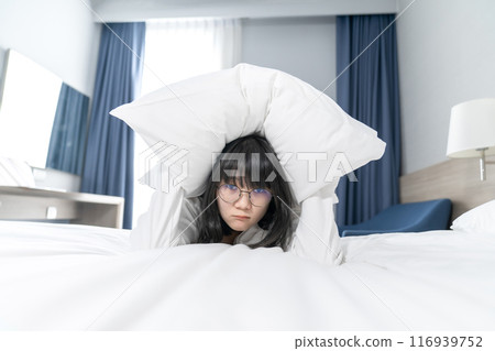 The Asian Pretty glasses woman feels afraid and uncomfortable, she holds white pillow to cover her head on the bed 116939752