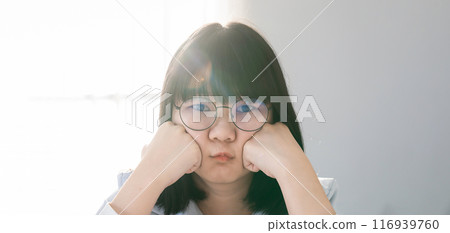 Pretty Asian Woman pucker up her lip in front of the bed in hotel bedroom, with the light from window curtain behind her. Pretty Asian Woman pucker up her lip in front of the bed in hotel bedroom, with the light from window curtain behind her. 116939760
