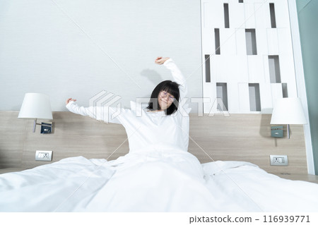 Little Asian young Glasses Girl stretches oneself on the bed in the morning with refreshing and happiness. 116939771