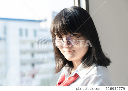 Asian glasses cute woman in blue shirt beside the curtain and window light in bedroom. Asian glasses cute woman in blue shirt beside the curtain and window light in bedroom. 116939779