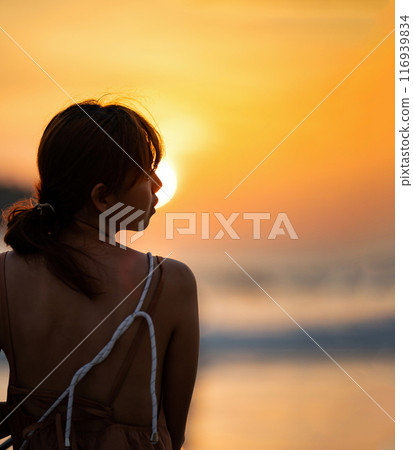 Asian Woman in Silhouette mood and tone of picture with orange warm sunset blurs, background on Kata Beach, Phuket province, Thailand. 116939834