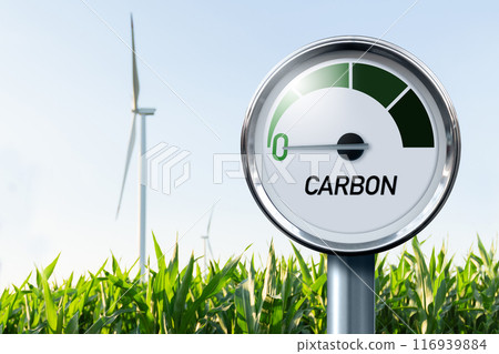 Gauge with inscription CARBON. Arrow points to zero. Agricultural field and wind turbines in the background. Concept of carbon neutral bio fuel 116939884