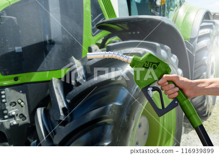 Hand with biofuel refueling nozzle on a background of agricultural tractor 116939899