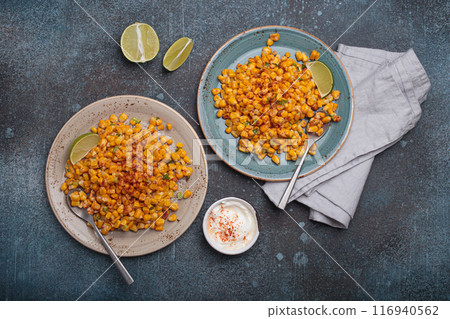 Two plates of esquites mexican street corn salad with chili, mayonnaise, and lime on dark stone background Two plates of esquites mexican street corn salad with chili, mayonnaise, and lime on dark stone background 116940562