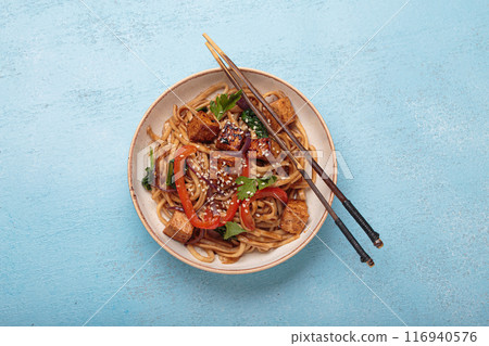 Bowl of vegetarian udon noodles with fried tofu and vegetables is served with chopsticks 116940576