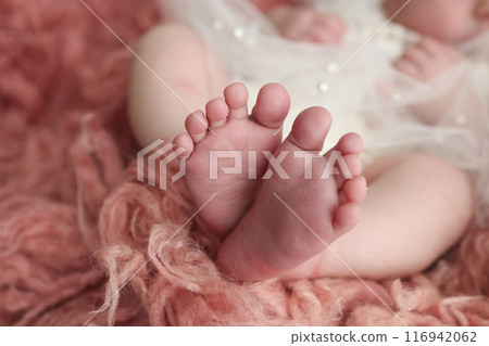The tiny foot of a newborn. Soft feet of a newborn in a pink red flakatti. Close up of toes, heels and feet of a newborn baby.Openwork white dress. Studio Macro photography. Woman's happiness. The tiny foot of a newborn. Soft feet of a newborn in a pink red flakatti. Close up of toes, heels and feet of a newborn baby.Openwork white dress. Studio Macro photography. Woman's happiness. 116942062