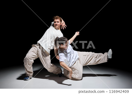 Dynamic image of young energetic people, man and woman in light casual clothes, dancing hip-hop against black studio background 116942409