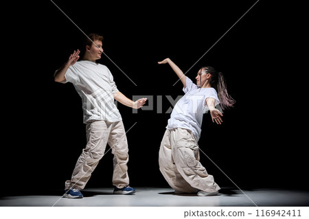 Freestyle. Imagination. Young talented man and woman in light clothes dancing hip-hop against black studio background 116942411
