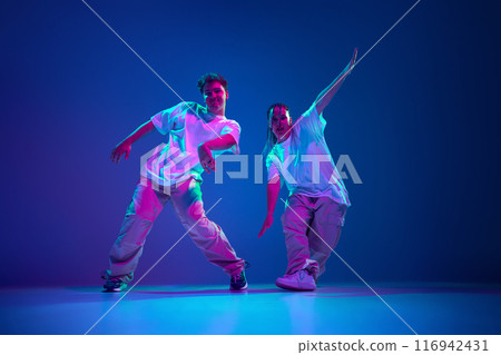 Flexible and energetic young people, man and woman dancing hip-hop, performing with passion against purple studio background in neon light Flexible and energetic young people, man and woman dancing hip-hop, performing with passion against purple studio background in neon light 116942431