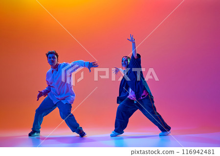 Modern dance school. Young people, man and woman in casual clothes dancing energetically hip-hop against gradient studio background in neon light 116942481