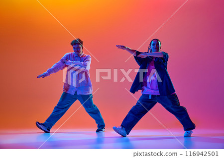 Artistic, talented young man and woman in casual clothes dancing hip-hop against gradient studio background in neon light 116942501