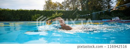 Banner. Wearing white cap and goggles, swimmer perfects his technique with yellow paddle in sunlit outdoor pool. Negative space. 116942516