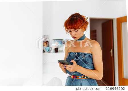 portrait of red-haired young woman wearing denim dress using phone portrait of red-haired young woman wearing denim dress using phone 116943202