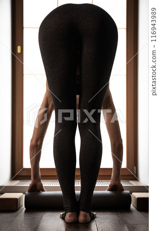 Slender female non-personalized figure from back in tilt hands touching floor while stretching yoga Slender female non-personalized figure from back in tilt hands touching floor while stretching yoga 116943989