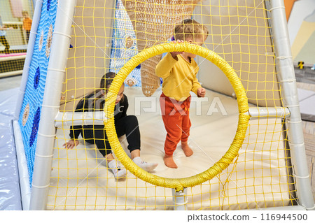 Two children on an indoor playground, unrecognizable children sitting in a maze. A modern colorful mesh playhouse for children in the mall. With space to copy. High quality photo Two children on an indoor playground, unrecognizable children sitting in a maze. A modern colorful mesh playhouse for children in the mall. With space to copy. High quality photo 116944500