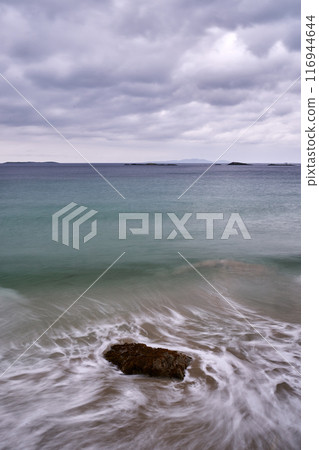 long exposure beach waves around rock cloudy day 116944644