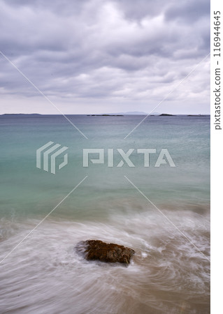 long exposure beach waves around rock cloudy day 116944645