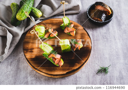 Delicious canapes of cucumber, red fish and dill on a board on the table Delicious canapes of cucumber, red fish and dill on a board on the table 116944690