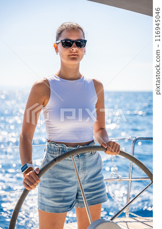 Young woman female captain stands at the helm and controls a sailboat during a journey by sea 116945046