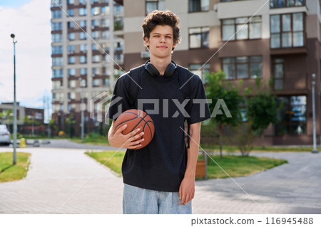 Young male with backpack basketball ball looking at camera outdoors, modern city Young male with backpack basketball ball looking at camera outdoors, modern city 116945488