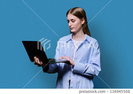 Smiling teenage girl with laptop on blue studio background 116945508