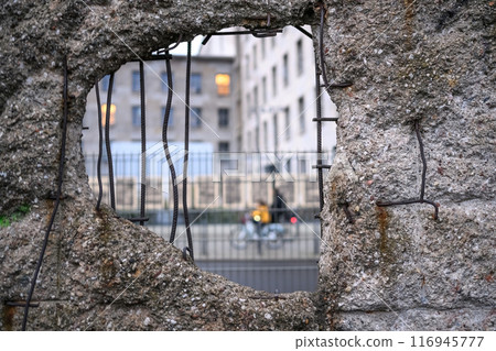 Hole in Broken Berlin wall and walking person against 116945777