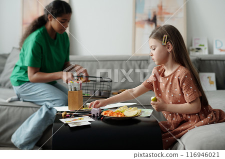 Girl with piece of apple taking crayon 116946021