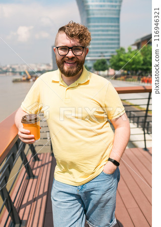 Bearded millennial man holding coffee to take away at early morning in sunny park near river in Belgrade city Bearded millennial man holding coffee to take away at early morning in sunny park near river in Belgrade city 116946321