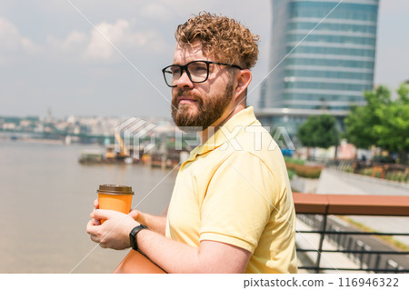 Bearded millennial man holding coffee to take away at early morning in sunny park near river in Belgrade city Bearded millennial man holding coffee to take away at early morning in sunny park near river in Belgrade city 116946322